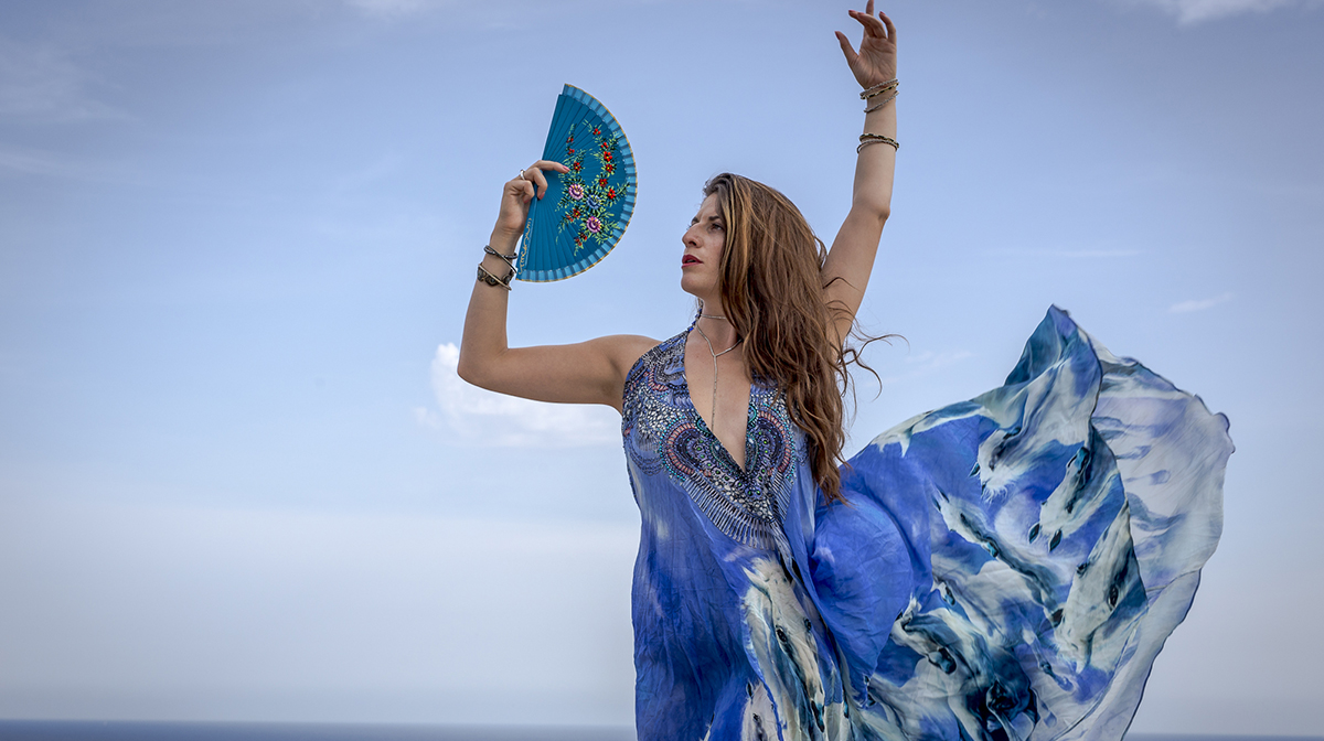 Tamar Ilana stands in a flamenco pose, holding a fan against the blue sky.